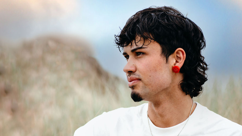 Young man at beach wearing red stud earrings with the word IA engraved into them.